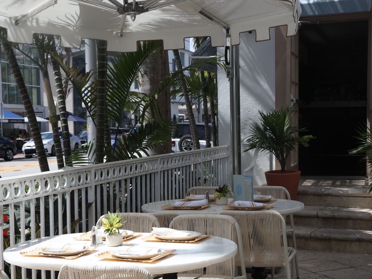 the shaded street-side terrace with set tables and palm trees