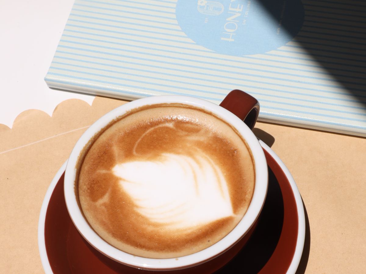 a cappuccino with latte art next to the Honey's menu
