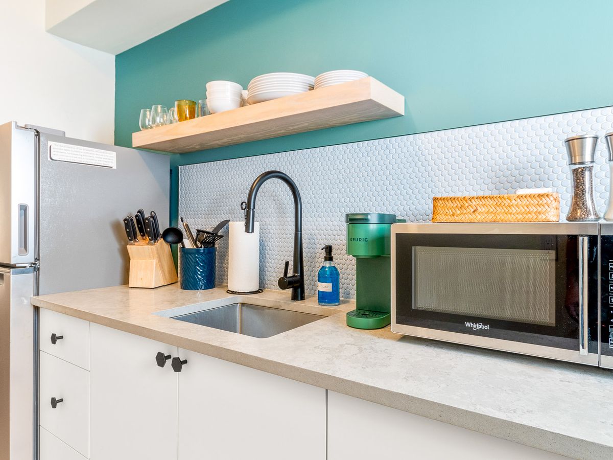 a kitchenette with a microwave, sink and open shelves